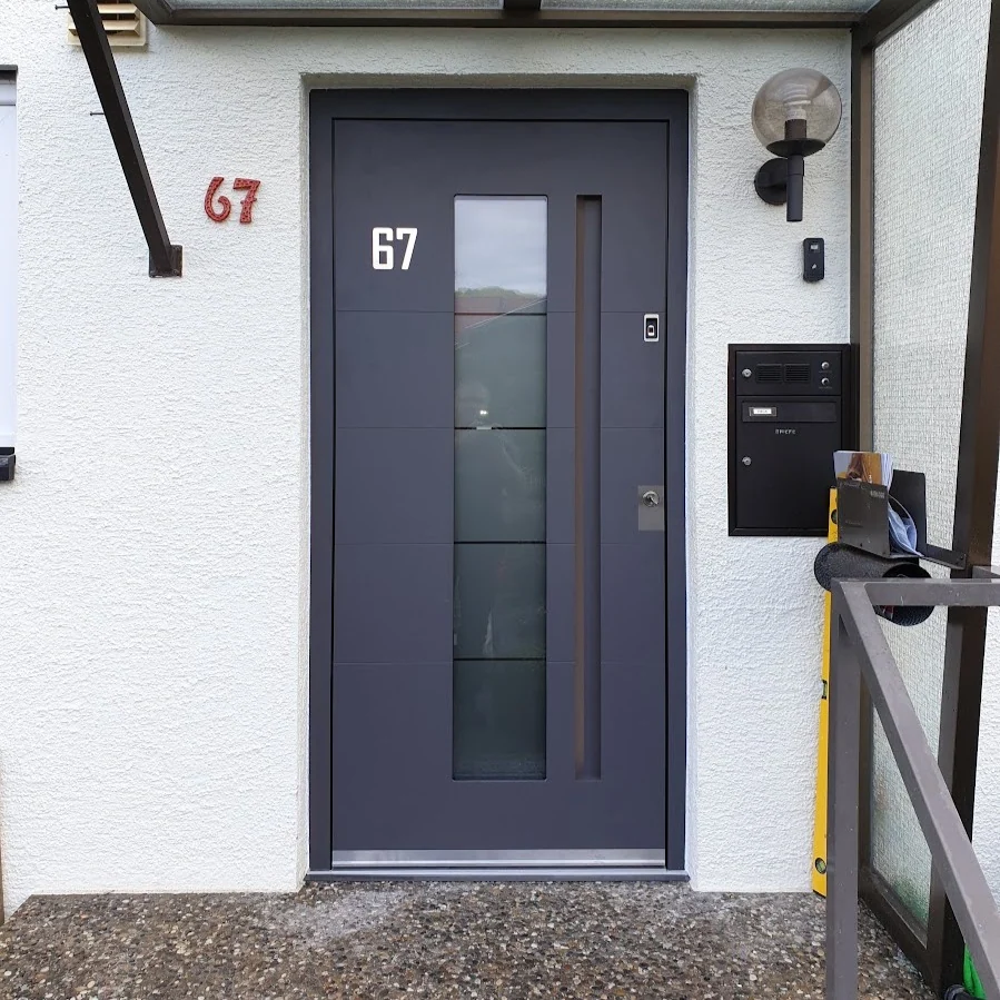 Graue Haustür mit Glasfeld und Hausnummer unter Vordach