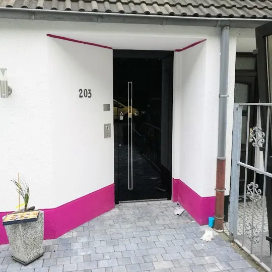 Schwarze Ganzglas Haustür mit Edelstahl-Stoßgriff an farbenfroh saniertem Haus